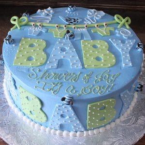 BB-016: Round blue cake with green and white polka-dot BABY letters, fondant bees, "Showers of Joy, It's a BOY!" in yellow and white script, and a white bead border at the base.