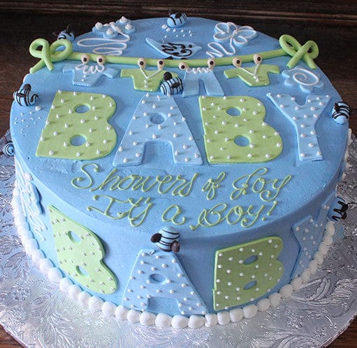 BB-016: Round blue cake with green and white polka-dot BABY letters, fondant bees, "Showers of Joy, It's a BOY!" in yellow and white script, and a white bead border at the base.