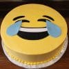The CB-005B is a round cake designed as the laughing face with tears emoji, topped with yellow frosting, a wide smiling mouth, and blue teardrops below the eyes.