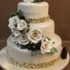 WD-264 is a three-tiered white cake adorned with white roses, pine cones, green leaves, and pearl-like accents in green and white, featuring textured bands on each tier and presented on a round ivory cake board.