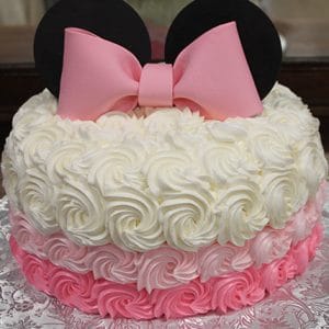The CB-001E is a round cake with white and pink rosette frosting, black fondant ears, and a large pink bow resembling Minnie Mouse, displayed on a silver-patterned board.