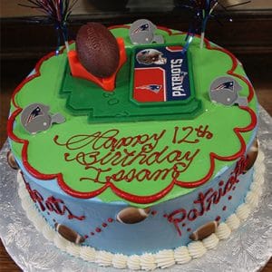 Celebrate with the SC-053 Patriots Football cake! Decorated in green and red with white trim, it features Patriots logos, a toy football, festive toppers, and “Happy 12th Birthday, Issam!” written in red.