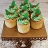 Six CC-075 chocolate cupcakes with white filling and holly berry decor are arranged on an ornate gold stand with crystal accents, set against a white floral surface and wooden background.