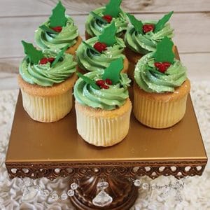 Vanilla cupcakes filled with CH-063B Gold cupcake/chocolate filling, topped with green frosting, red candy berries, and holly leaves, displayed on a crystal-accented gold stand against a white textured background.