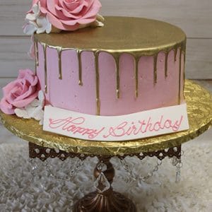 The BR-033 Gold Drip Pink cake features pink and gold drip icing, large pink and white sugar roses, and a "Happy Birthday" plaque in pink script, all presented on a gold cake stand with crystal accents.