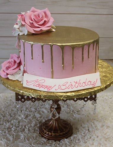 The BR-033 Gold Drip Pink cake features pink and gold drip icing, large pink and white sugar roses, and a "Happy Birthday" plaque in pink script, all presented on a gold cake stand with crystal accents.