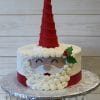 CH-024 is a round cake designed as Santa Claus, featuring a tall red hat, an icing white beard, smiling eyes, and a holly detail on the side, presented on a silver cake stand.
