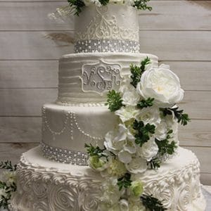 The WD-032 is a four-tiered white wedding cake featuring intricate piping, pearl-like accents, rhinestone bands, and cascading white flowers with greenery, displayed against a light wooden background.