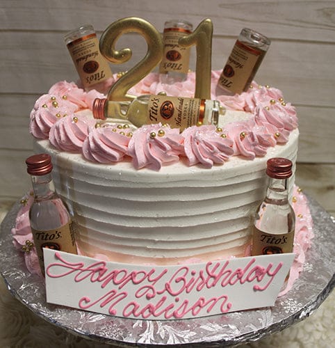 The BD-024M PinkTitos cake features white layers, pink frosting, gold beads, a gold 21 topper, and mini Tito’s vodka bottles. A plaque in pink script says "Happy Birthday Madison." The cake is displayed on a silver board.