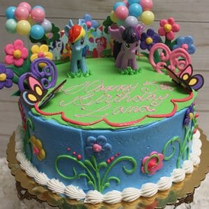 The SC-024 My Little Pony birthday cake features blue icing, floral and butterfly decorations, two pony figurines on top, and "Happy 5th Birthday Lana" in pink icing. Balloons and festive decorations surround the cake.
