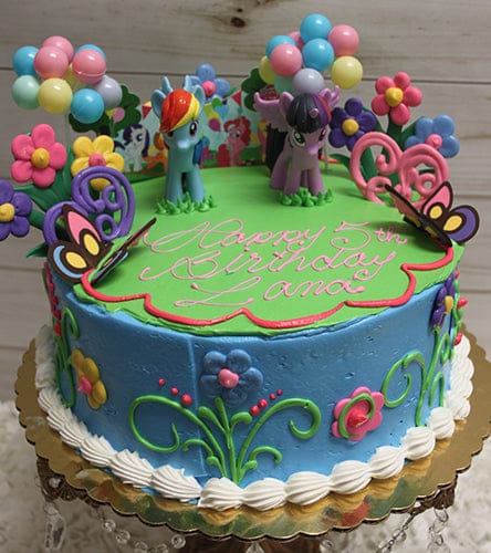 The SC-024 My Little Pony birthday cake features blue icing, floral and butterfly decorations, two pony figurines on top, and "Happy 5th Birthday Lana" in pink icing. Balloons and festive decorations surround the cake.