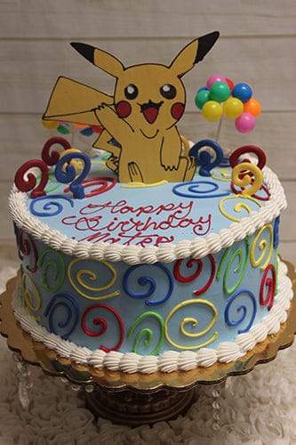 The SC-009 Pokemon cake is round with colorful swirls, candles, a Pikachu cutout topper, balloon decorations, and "Happy Birthday" written in red icing.