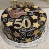 BD-063 Guitar/gold stars: Round chocolate cake with yellow stars, white swirls, a fondant guitar, and “Tom 50” in large gold letters on top, presented on a silver platter.