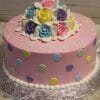 CB-031 is a round pink birthday cake with pastel polka dots, topped with icing roses in yellow, blue, purple, and pink, edged in white frosting pearls, and finished with a handwritten birthday message on top.