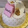 The BB-045 is a quilted white cake with gold pearl accents, featuring a pink book labeled Baby & Co, a gold teddy bear, a white bib with Baby & Co, and a gold rattle, all presented on a gold platter.