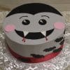 The HW-008 is a round cake designed as a cartoon vampire face with fangs, pink cheeks, and dripping blood. Icing bats decorate the sides, a red ribbon trims the base, and it rests on a silver-patterned board.