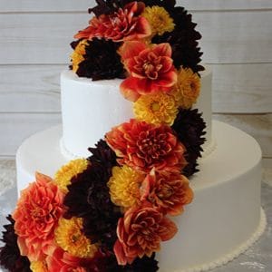The WD-088 features two white tiers adorned with cascading orange, yellow, and dark red flowers, presented on a silver cake board against a light wooden background.