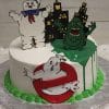 The CB-010A cake showcases the Stay Puft Marshmallow Man, Slimer, city buildings, and the Ghostbusters logo, with green icing dripping down one side and a green icing trim at the base.