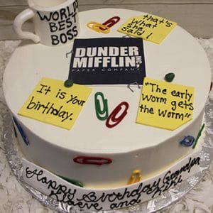 A round BD-136 cake features colorful paperclips, quote post-it notes, a Dunder Mifflin Paper Company logo, and a "World’s Best Boss" mug. The cake reads: "Happy Birthday Grandpa, We love you!.