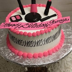 The BD-028C Make up cake features a round design with pink icing, a zebra-print band, fondant makeup toppers, and a pink “Happy Birthday Gemya” banner, all presented on a silver-wrapped stand.