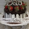 The FD-001 cake features chocolate drips, strawberries, a large “Dad” topper, and “Happy Father’s Day” written on a white plaque at the base, all displayed on a glass stand with a lace doily.