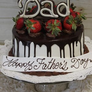 The FD-001 cake features chocolate drips, strawberries, a large “Dad” topper, and “Happy Father’s Day” written on a white plaque at the base, all displayed on a glass stand with a lace doily.