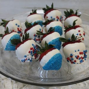 JC-020 White dipped strawberries with Fourth of July decor arranged on a clear glass plate, featuring blue sprinkles and red, white, and blue star-shaped sprinkles.