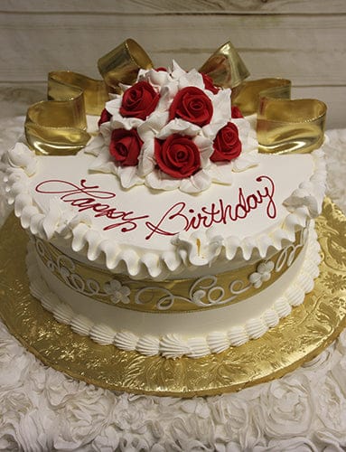 The AN-002A is a round birthday cake with white icing, gold ribbon accents, and red and white fondant roses on top. "Happy Birthday" in red script decorates the cake, which sits on a gold floral-patterned board.