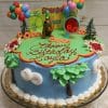 The SC-042 Scooby Doo is a colorful round birthday cake featuring Scooby-Doo themed toppers, balloon clusters, trees, and clouds, finished with “Happy Birthday Layla” written in red icing.