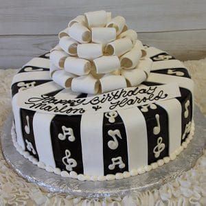 The BD-063 Ganache/Bow/Music notes cake features black and white vertical stripes, white musical notes, a large white bow on top, and a birthday message for Marlon and Harold on a white plaque.