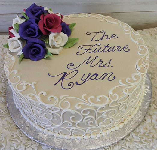 The BR-023 is a round cake with white icing swirls, purple, red, and white fondant roses on top, and “The Future Mrs. Ryan” written in purple script.