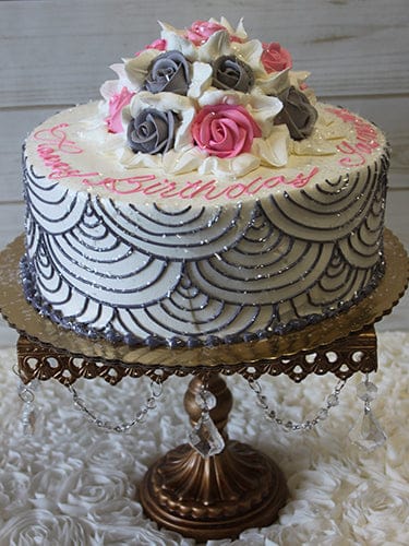 BR-013 is a round white cake with gray and pink roses on top, gray scalloped icing on the sides, and pink writing. It's displayed on an ornate gold stand with crystal accents against a white textured background.