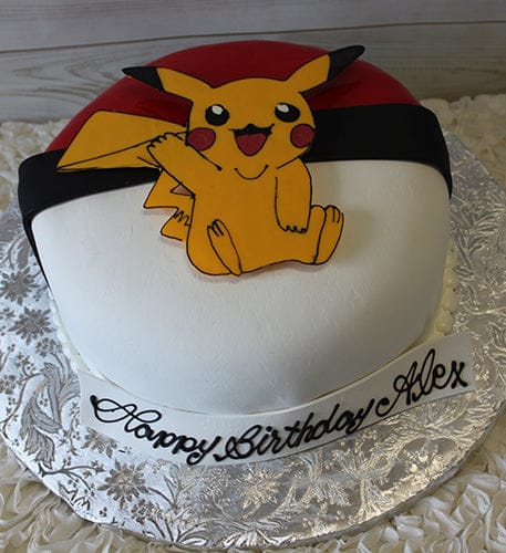 The CB-011Q is a round Poké Ball-themed cake topped with an icing Pikachu and a white plaque reading "Happy Birthday Alex" in cursive. It’s displayed on a silver floral-patterned board.