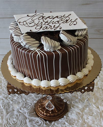 The BD-013A chocolate Oreo cake features white icing drizzles, chocolate-dipped cookies on top, and a white “Happy Birthday Gary” plaque, displayed on a gold stand with crystal accents.