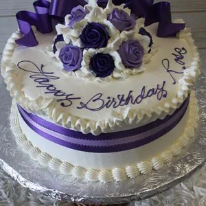 The AN-007 is a round white cake topped with purple and white roses, a purple ribbon, and "Happy Birthday Love" in purple icing. Presented on a silver platter.