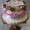 The AN-001 birthday cake features white and pink frosting, strawberries, pink roses, and green leaves atop a gold cake stand. A white plaque with "Happy Birthday" in pink decorates the top.