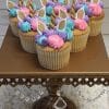 Six unicorn-themed cupcakes with pastel pink, purple, and blue frosting, gold unicorn horns, and white ears are displayed on an ornate gold cake stand with crystal decorations.
