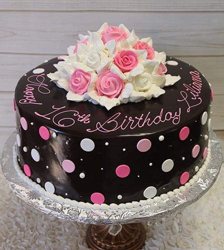 BD-158: A round chocolate cake with pink and white polka dots, topped with a bouquet of pink and white roses, featuring “Happy 16th Birthday Liliana” in pink script icing.