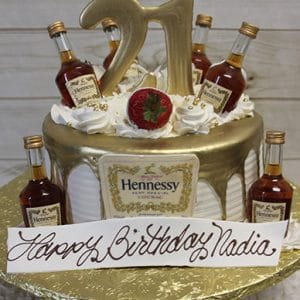 The BD-024J HennessywithNumber birthday cake features mini Hennessy bottles, gold accents, a large gold 21 topper, white frosting, a strawberry, and a “Happy Birthday Nadia” cursive sign.