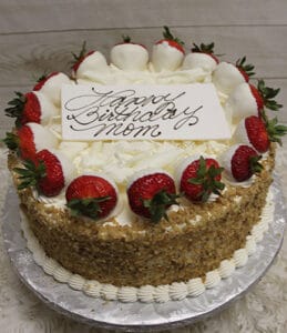 A round BD-008C Carrot cake with white frosting, crushed nuts on the sides, and strawberries dipped in white chocolate. A white card on top says “Happy Birthday mom” in elegant script.