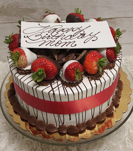 The BD-000C WHITE AND DARK DIPPED STRAWBERRIES is a round cake with a red ribbon, chocolate drizzle, chocolate shavings, and strawberries dipped in white and dark chocolate. A white plaque reads Happy Birthday Mom in elegant script.