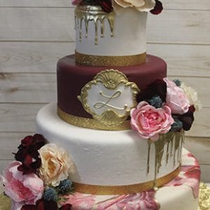 WD-090 features three tiers with gold accents, burgundy and white layers, pink and cream flowers, gold drip details, a marbled pink bottom tier, and a gold monogram "L" on the middle tier.