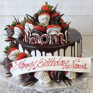 A chocolate-dripped cake (BD-065) topped with chocolate-covered strawberries features the name Naomi in white and red letters. A white plaque reads "Happy Birthday Naomi" in red script.