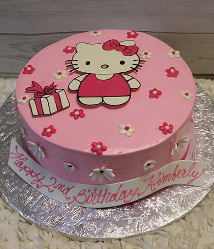The CB-009W is a pink birthday cake with a Hello Kitty figure, white and pink flowers, a gift box, and “Happy 2nd Birthday Kimberly” written in pink icing on the side.