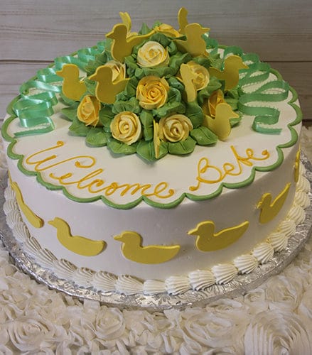 BB-009 is a round white cake topped with yellow duck shapes, green and yellow icing roses, yellow icing butterflies, and "Welcome Bebe" written in yellow icing.