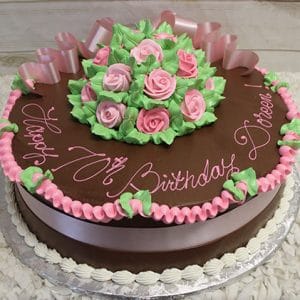 The AN-010 is a round chocolate cake with pink and green icing roses, a pink ribbon and border, "Happy 70th Birthday Doris!" written in pink icing, and presented on a silver tray.