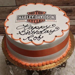 The GR-003 is a round cake featuring the Harley-Davidson logo, orange and white icing, an orange ribbon on the side, and “Happy Birthday Rob” in black icing. Presented on a gold tray.