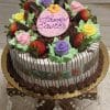 The Strawberry Grand Marnier cake with Easter Decor features chocolate-dipped strawberries, pastel icing roses, green icing leaves, and a large pink oval reading "Happy Easter," all presented on a golden stand with crystal accents.