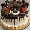 The BD-024A Baileys is a round cake with white frosting, chocolate drip, cream swirls, chocolate-covered strawberries, and mini Baileys bottles on top, presented on a gold-edged cake board.
