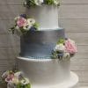 WD-095 is a four-tiered wedding cake featuring white, pink, and blue flower decorations, light blue accents on the second tier, and a Mr & Mrs topper, set against a wooden background.